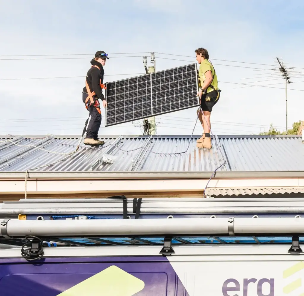 Erg Energy installers carrying a solar panel above the company van